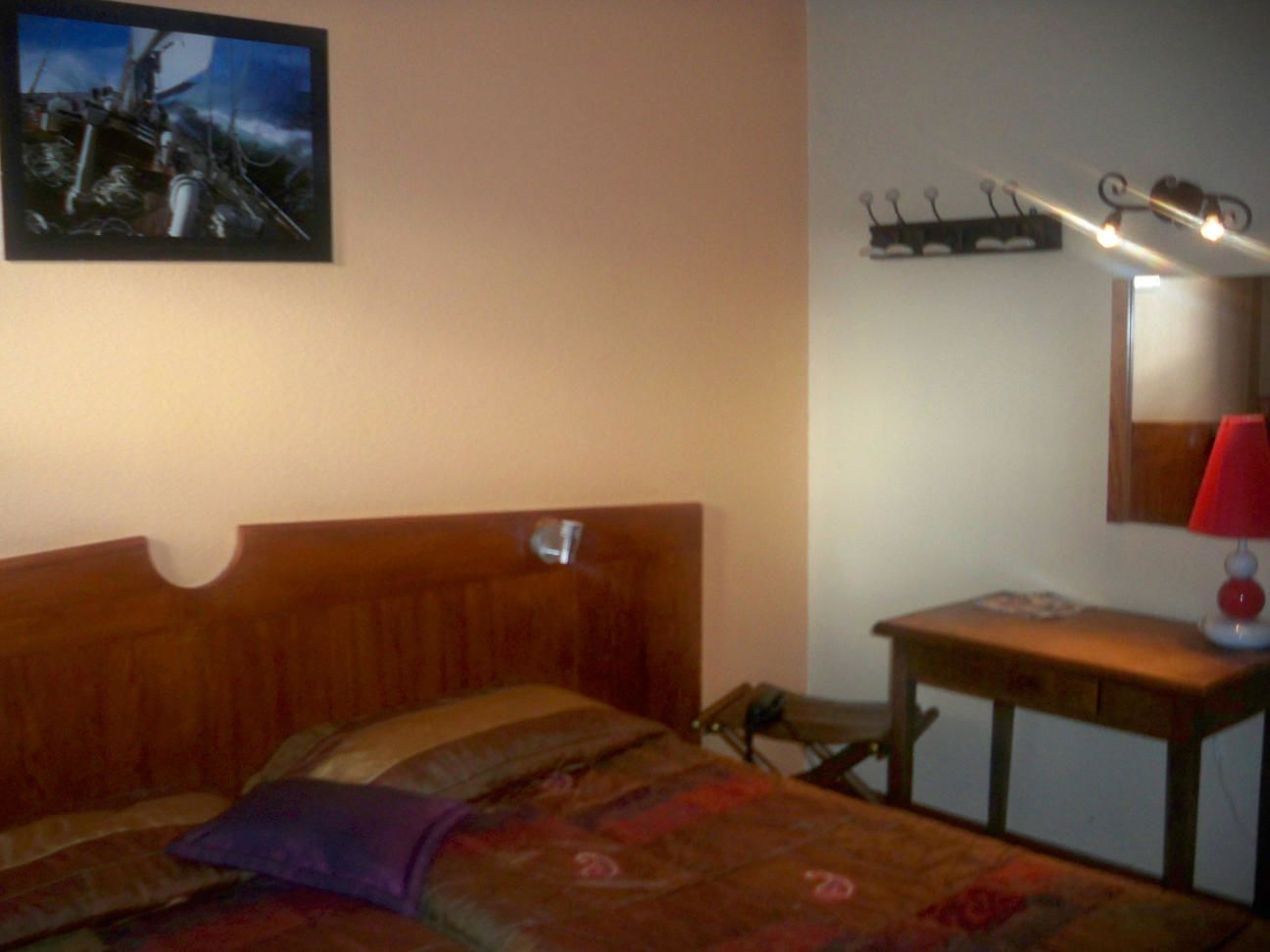 Un dormitorio con cama de madera, una mesita de noche con lámpara, un estante en la pared y un cuadro sobre la cama.