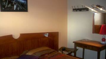 Un dormitorio con cama de madera, una mesita de noche con lámpara, un estante en la pared y un cuadro sobre la cama.