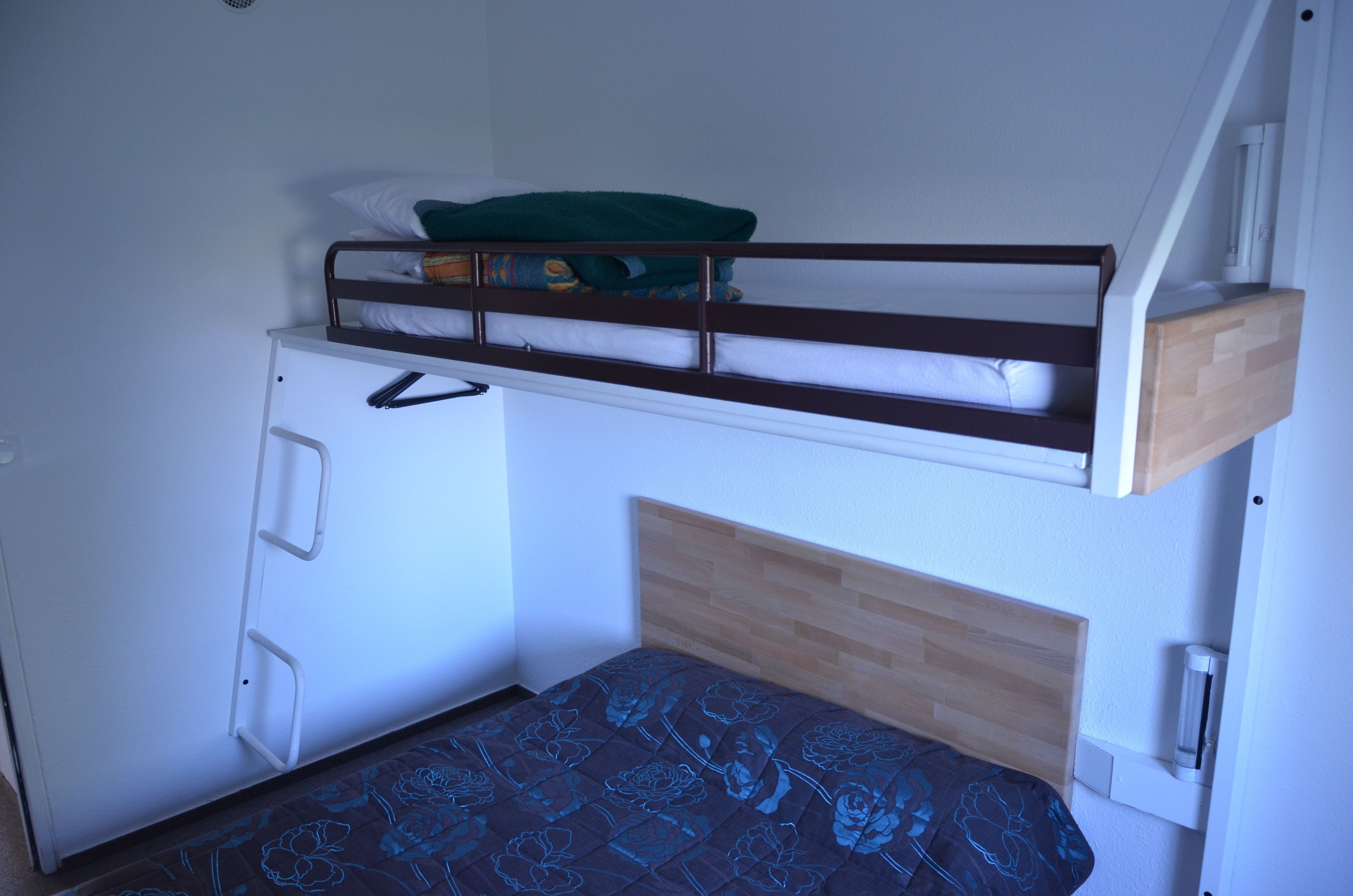 Een stapelbed met een houten hoofdbord en een onderbed met een bedspread met een patroon.