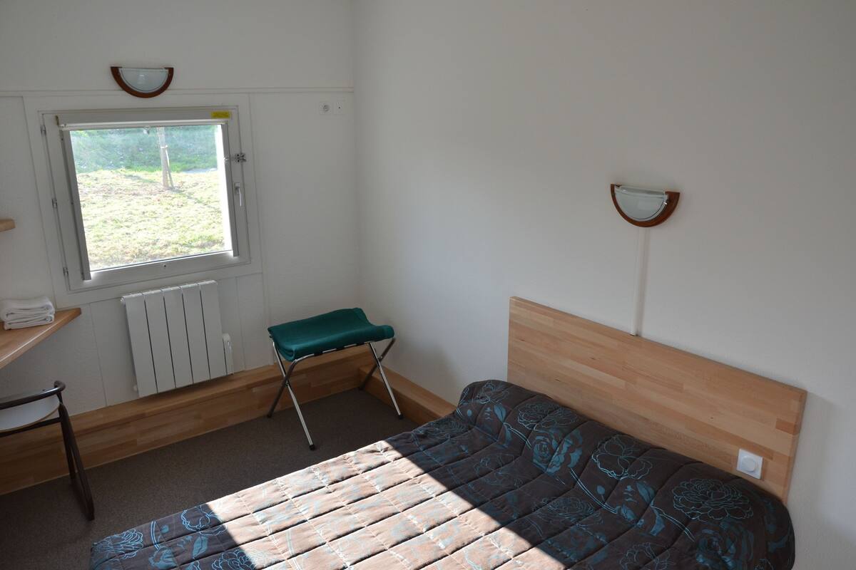 A small, clean room with a single bed, a window, a radiator, a chair, and a small table.