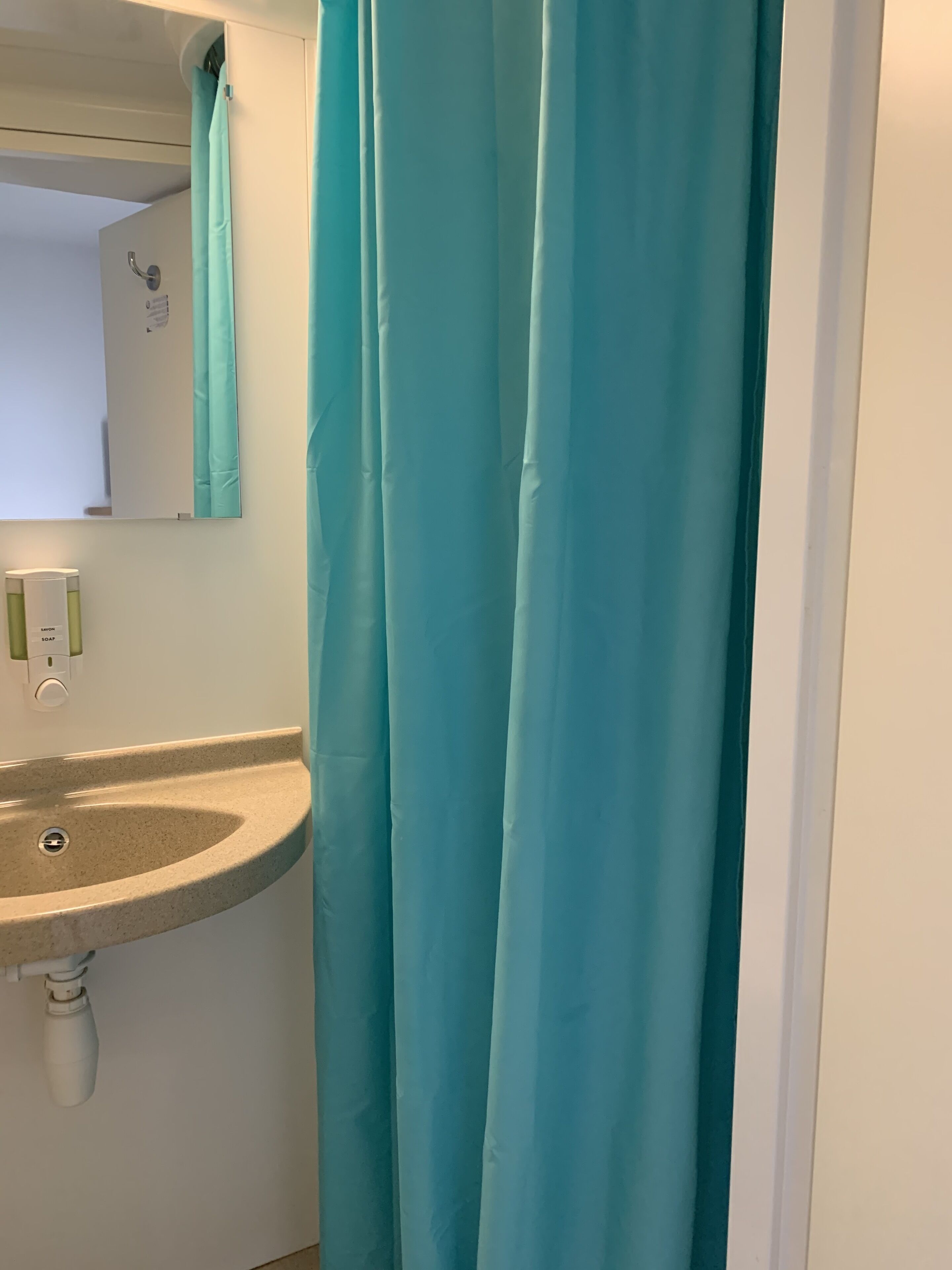 Ein Badezimmer mit Waschbecken, Spiegel und einem türkisfarbenen Duschvorhang.