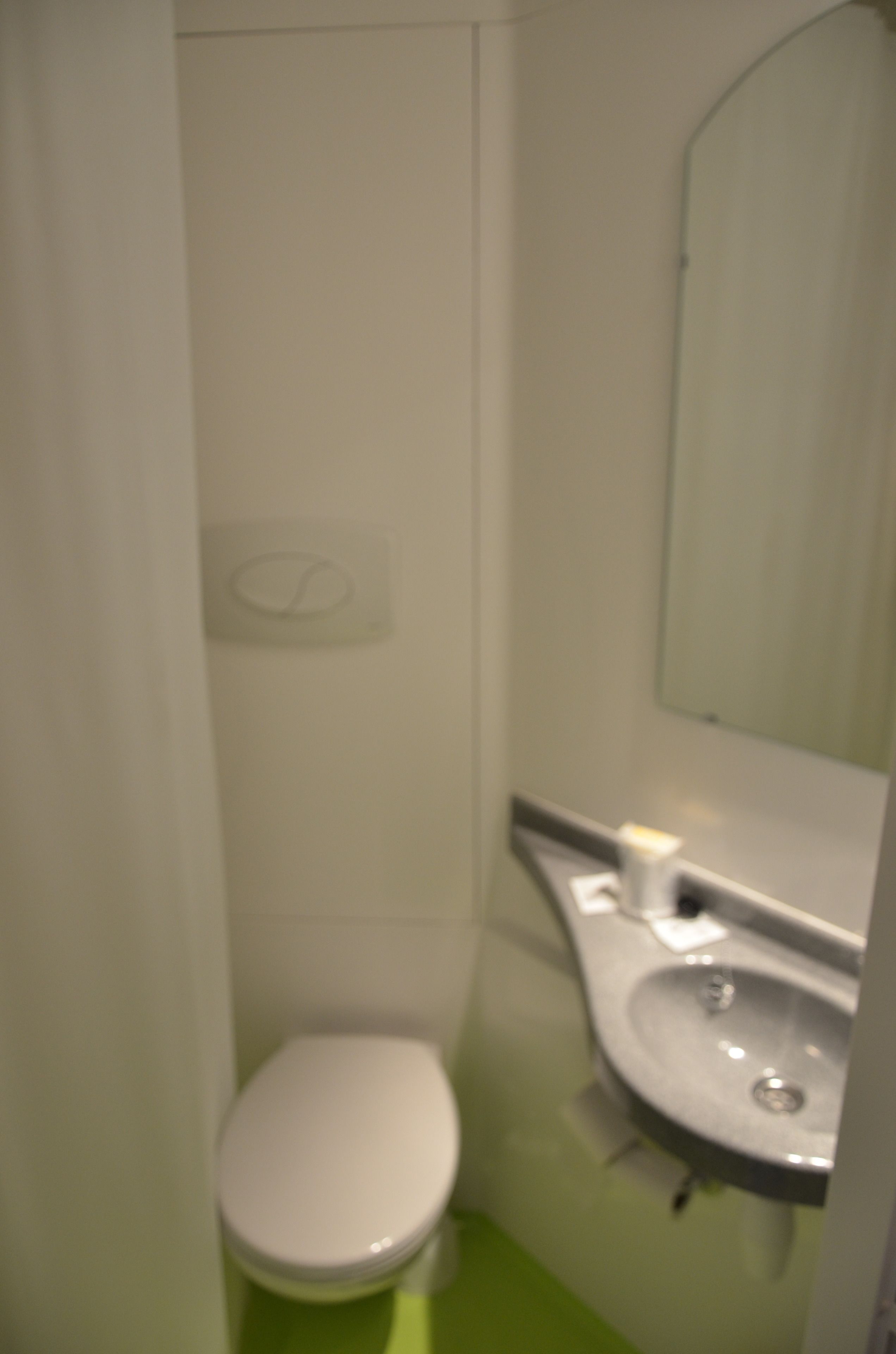 Et lille, kompakt badeværelse med et hvidt toilet, en vask og et spejl.
