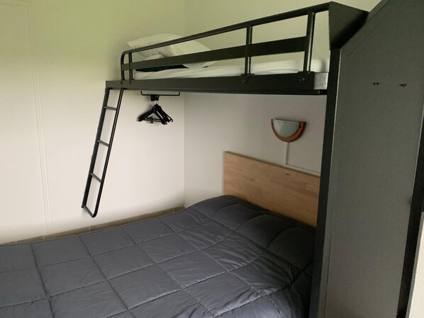 Una cama litera con escalera, un cabecero de madera, un espejo montado en la pared y un perchero.