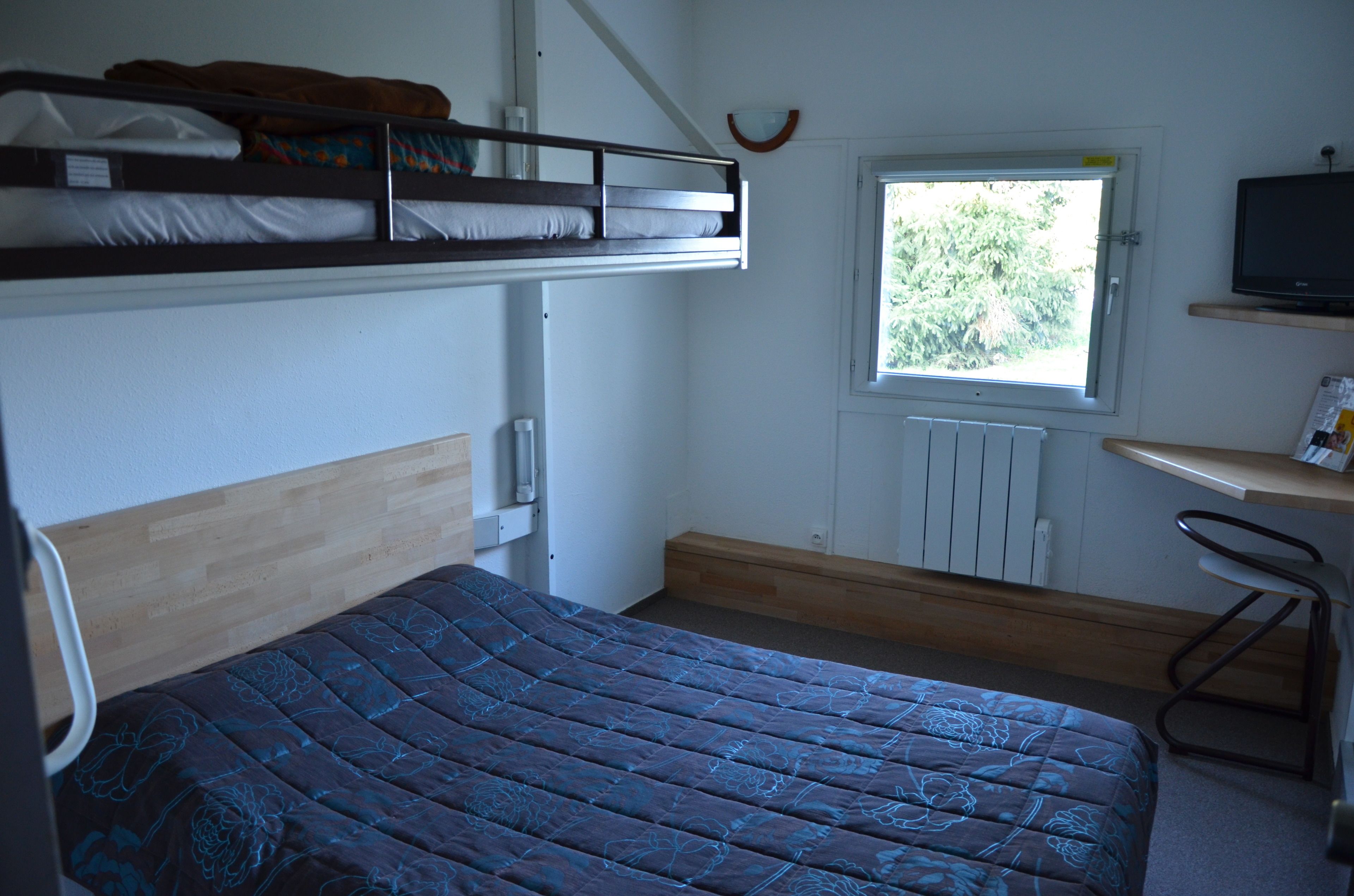 Habitación pequeña con una litera, un escritorio con silla y ventana con vistas a árboles.