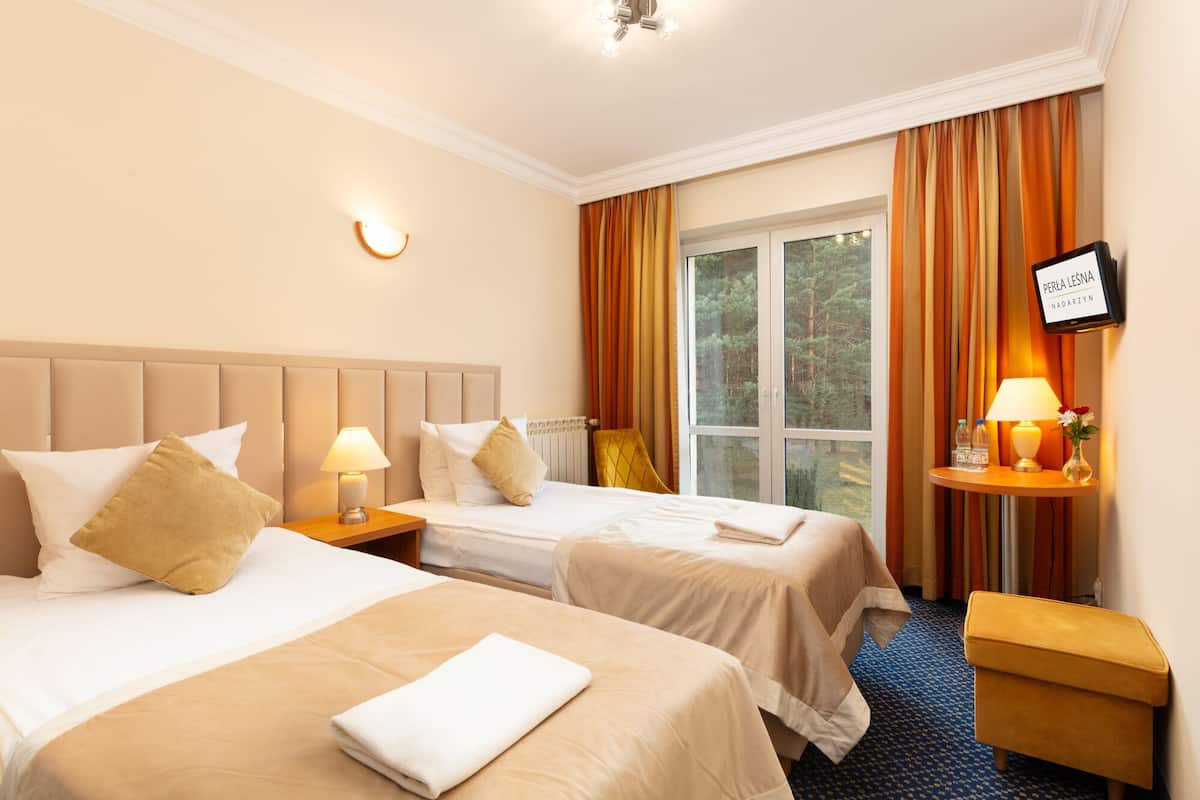 A hotel room with two beds, a small table with a lamp, a window with curtains, and a sign on the wall.