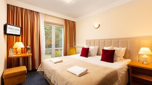 Habitación de hotel con una cama grande, dos mesitas de noche, un televisor y una ventana con cortinas.