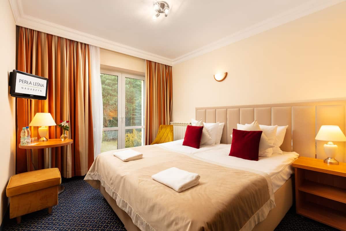 A hotel room with a large bed, two bedside tables, a TV, and a window with curtains.