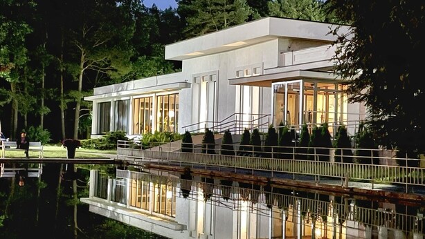 Una casa moderna de dos pisos con ventanas amplias y una piscina reflectante al frente.