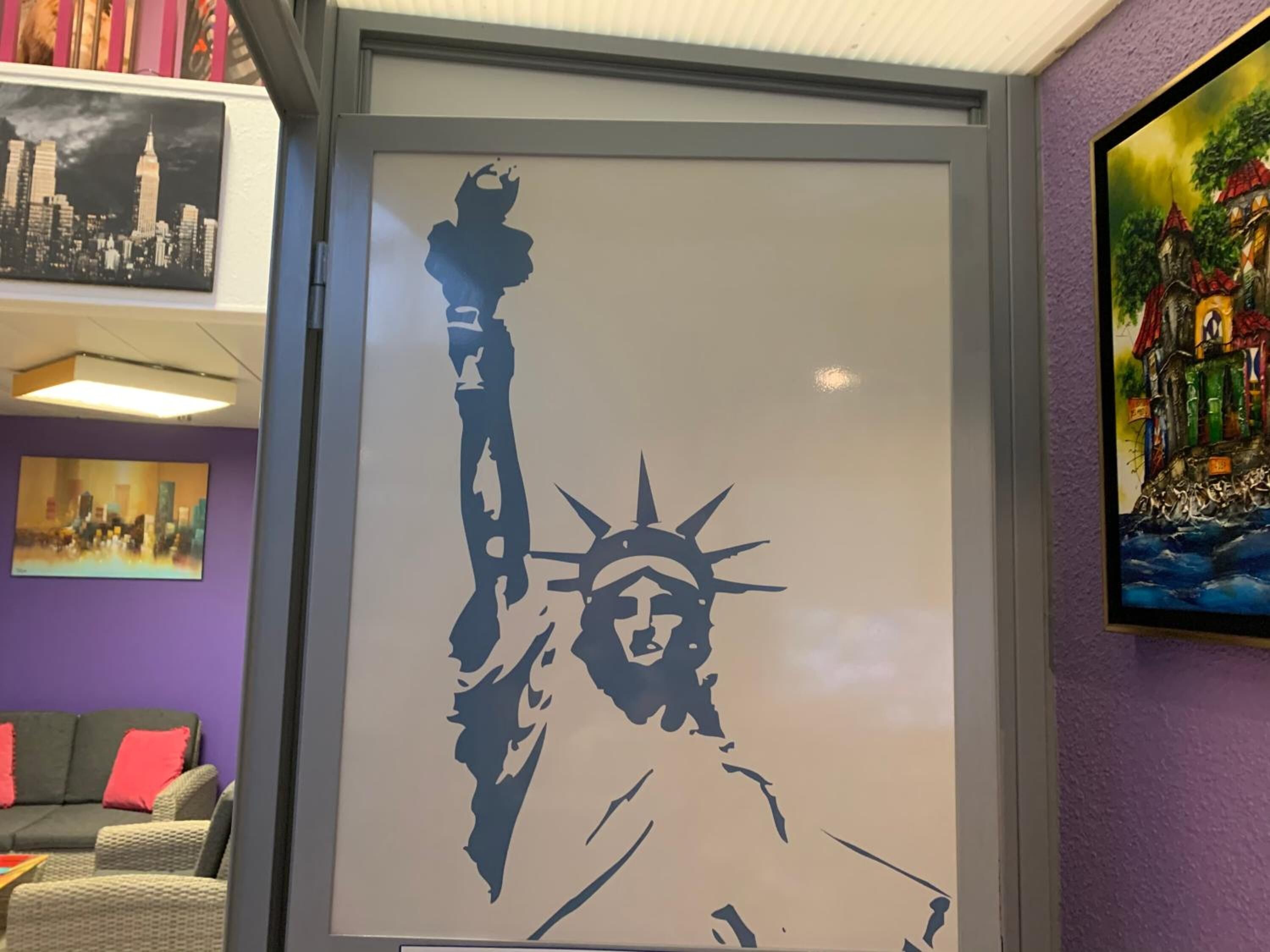 Une silhouette encadrée de la Statue de la Liberté, dans une pièce aux murs violets, avec un canapé et un tableau représentant un château.