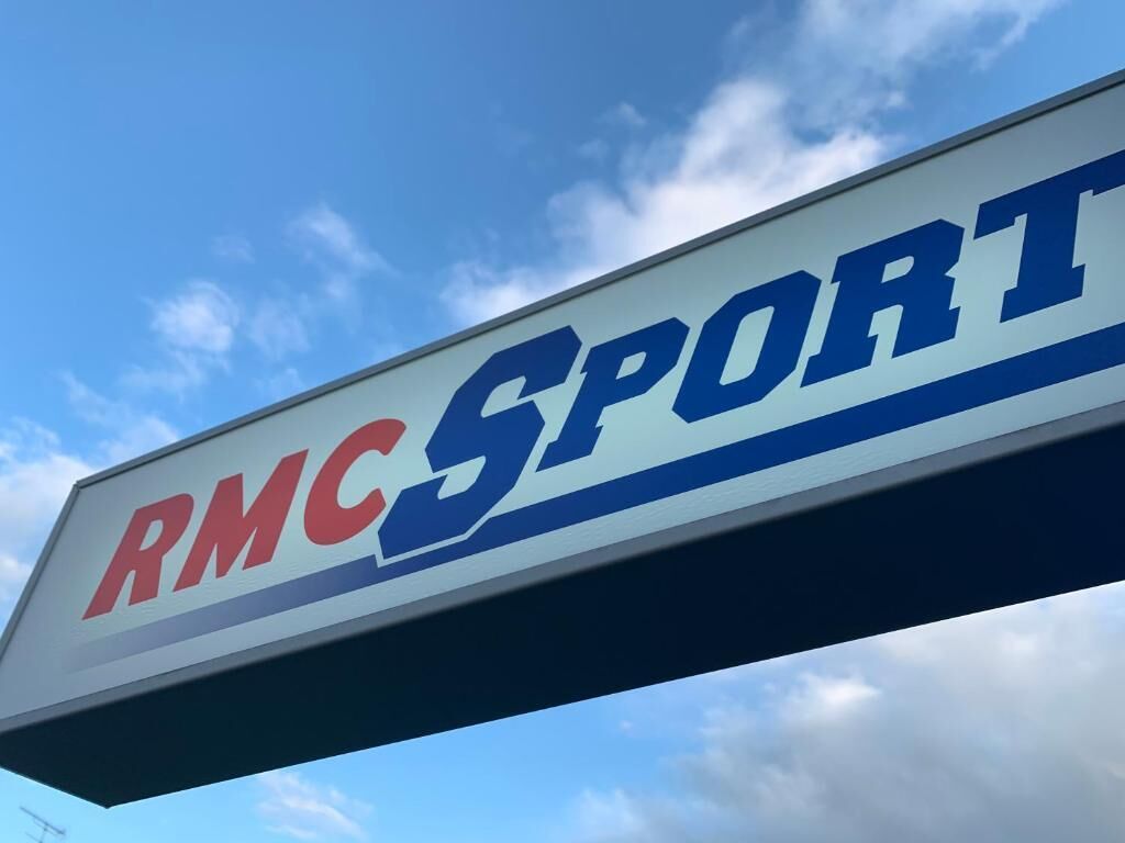 Une enseigne avec l’inscription « RMC SPORT » sur un fond de ciel bleu.
