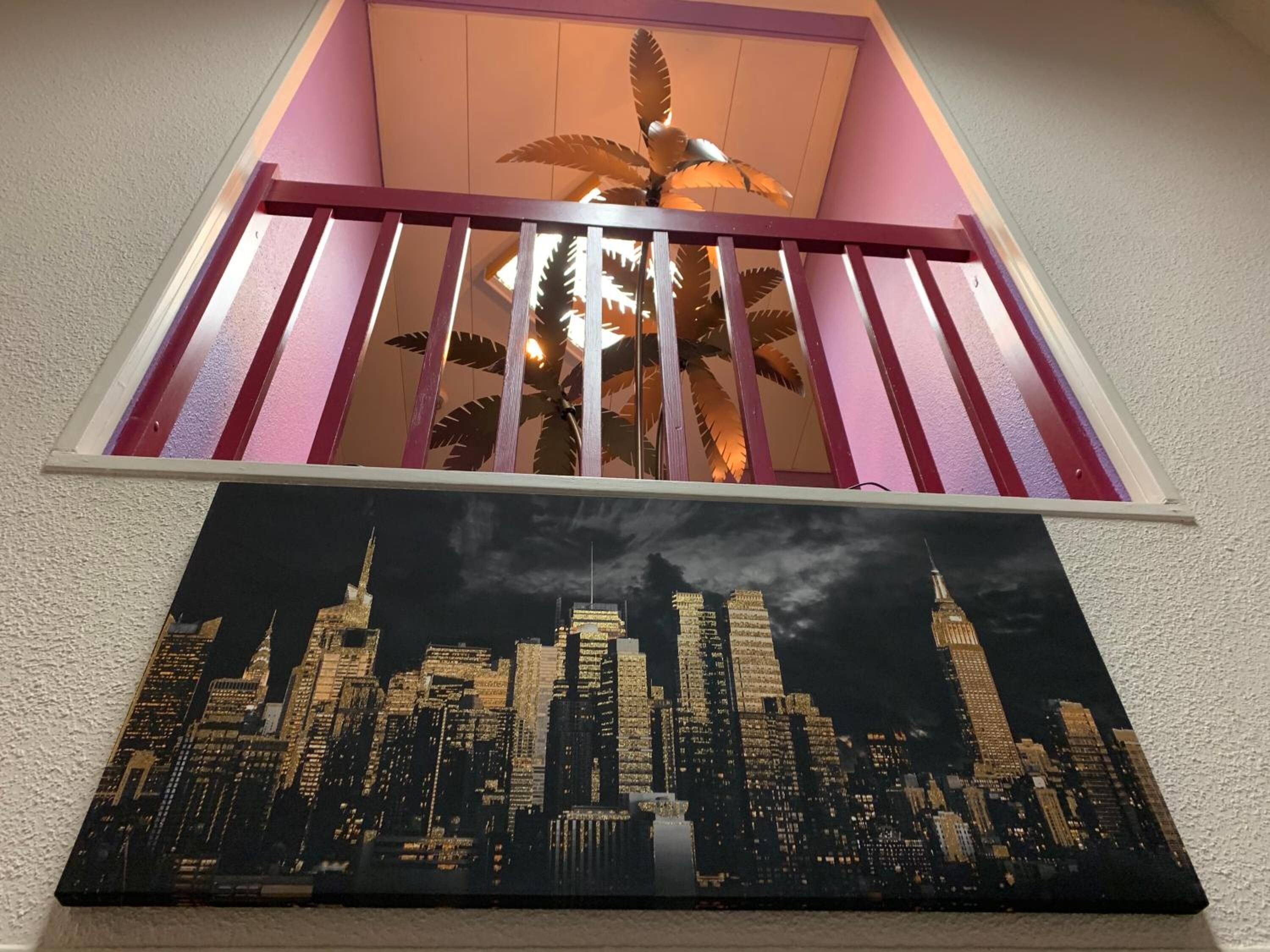 Un escalier avec une rampe, un luminaire au plafond et un tableau représentant un paysage urbain accroché au mur.