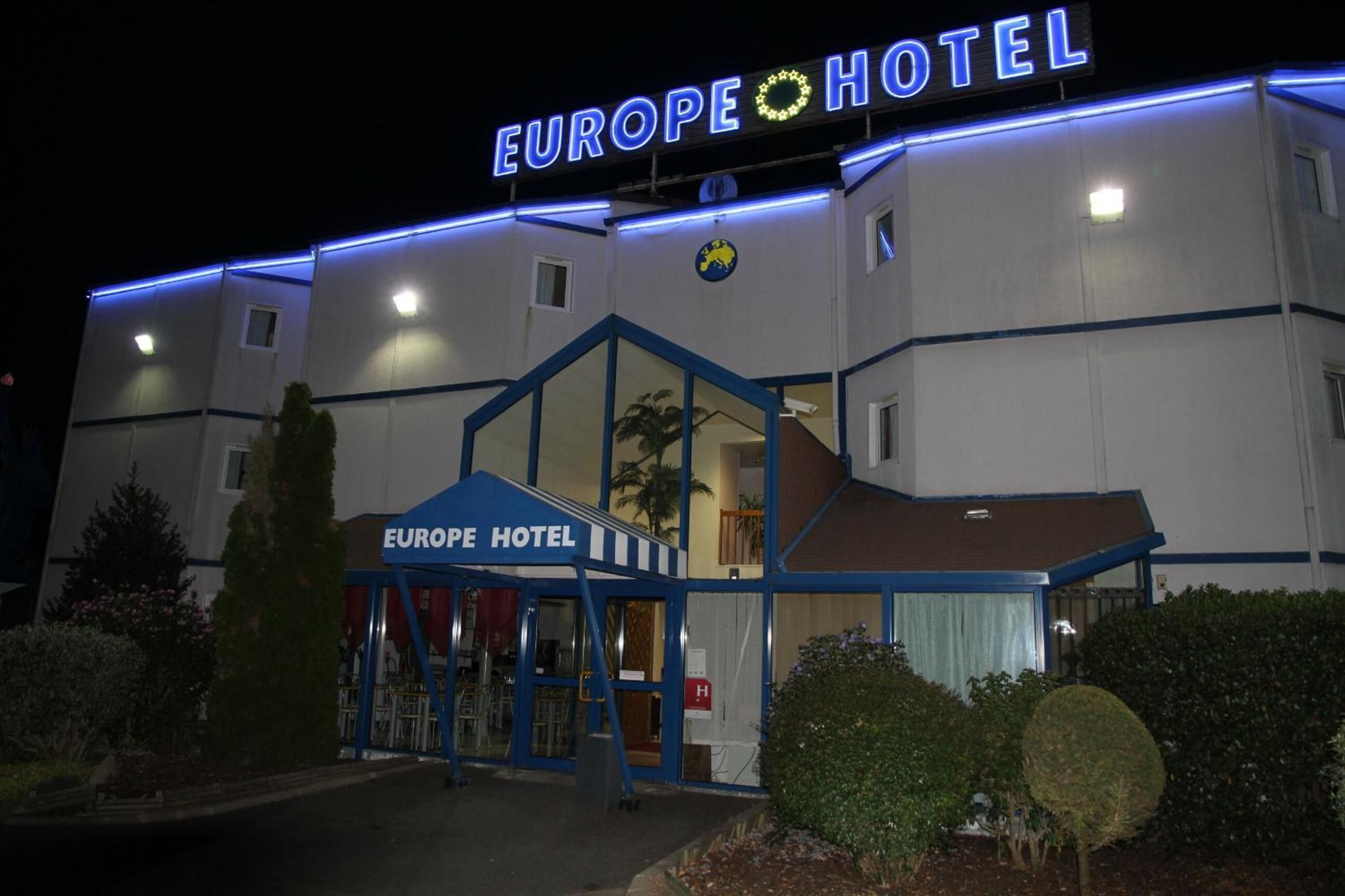 De gevel van Hotel Europa, met een opvallend neonbord, een glazen ingang en een blauw luifel.