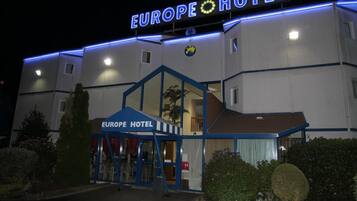 De gevel van Hotel Europa, met een opvallend neonbord, een glazen ingang en een blauw luifel.