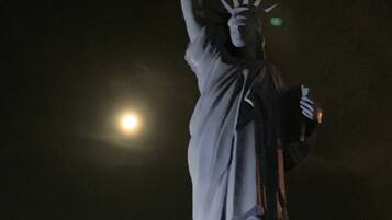 Vista noturna da Estátua da Liberdade, com uma lua cheia ao fundo.
