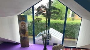 Een hotel lobby met een rood tapijt, een receptiebalie, een potplant en uitzicht op buiten.
