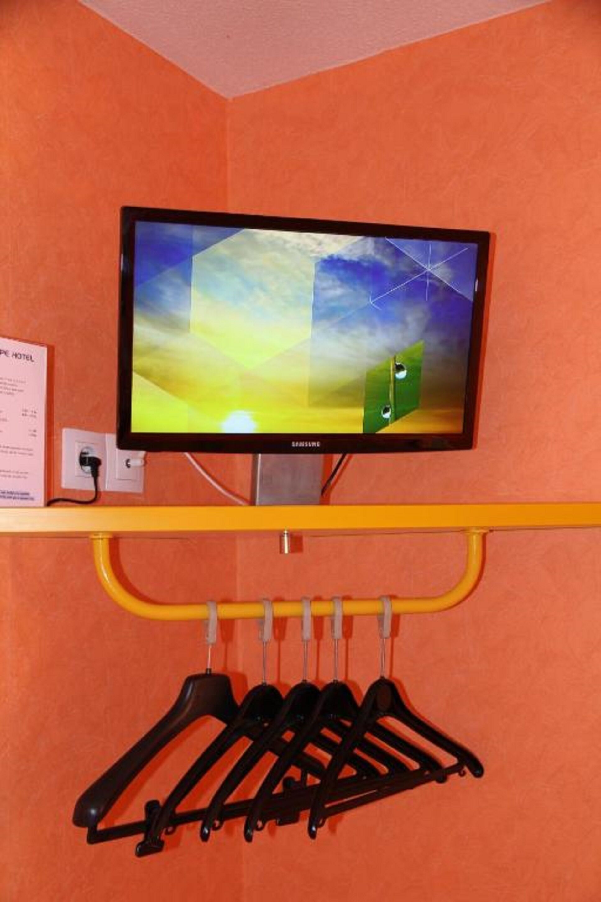 A Samsung TV mounted on a wall with a yellow shelf below it, holding several black hangers.