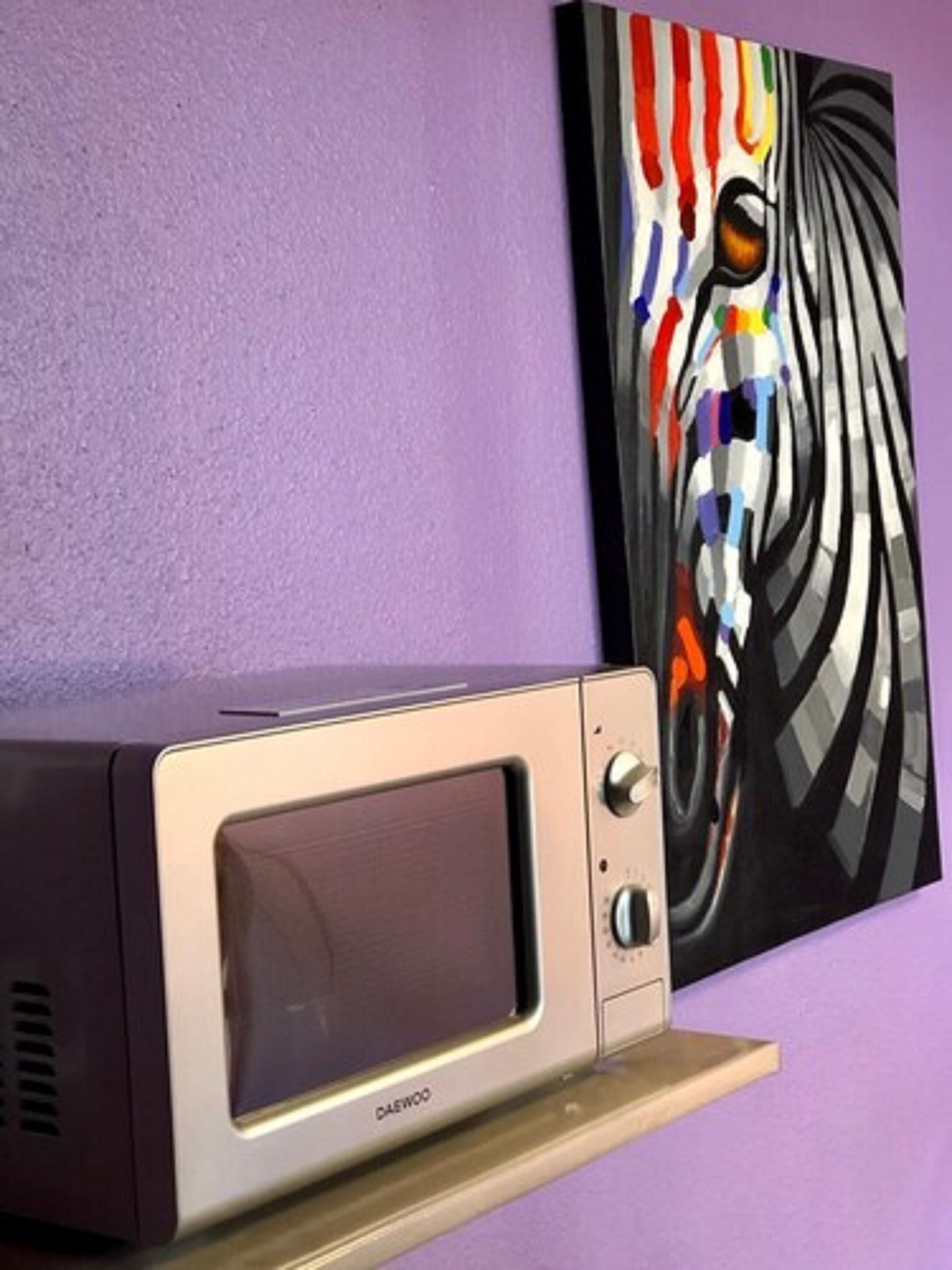 A microwave on a wooden shelf against a purple wall.