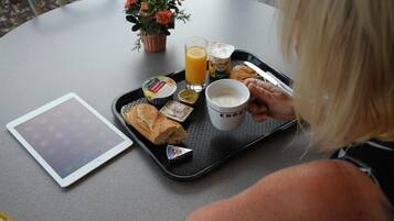 Ein Tablett mit Frühstücksartikeln, darunter Toast, Saft und eine Kaffeetasse, steht auf einem Tisch mit einem Tablet und einem Blumentopf.