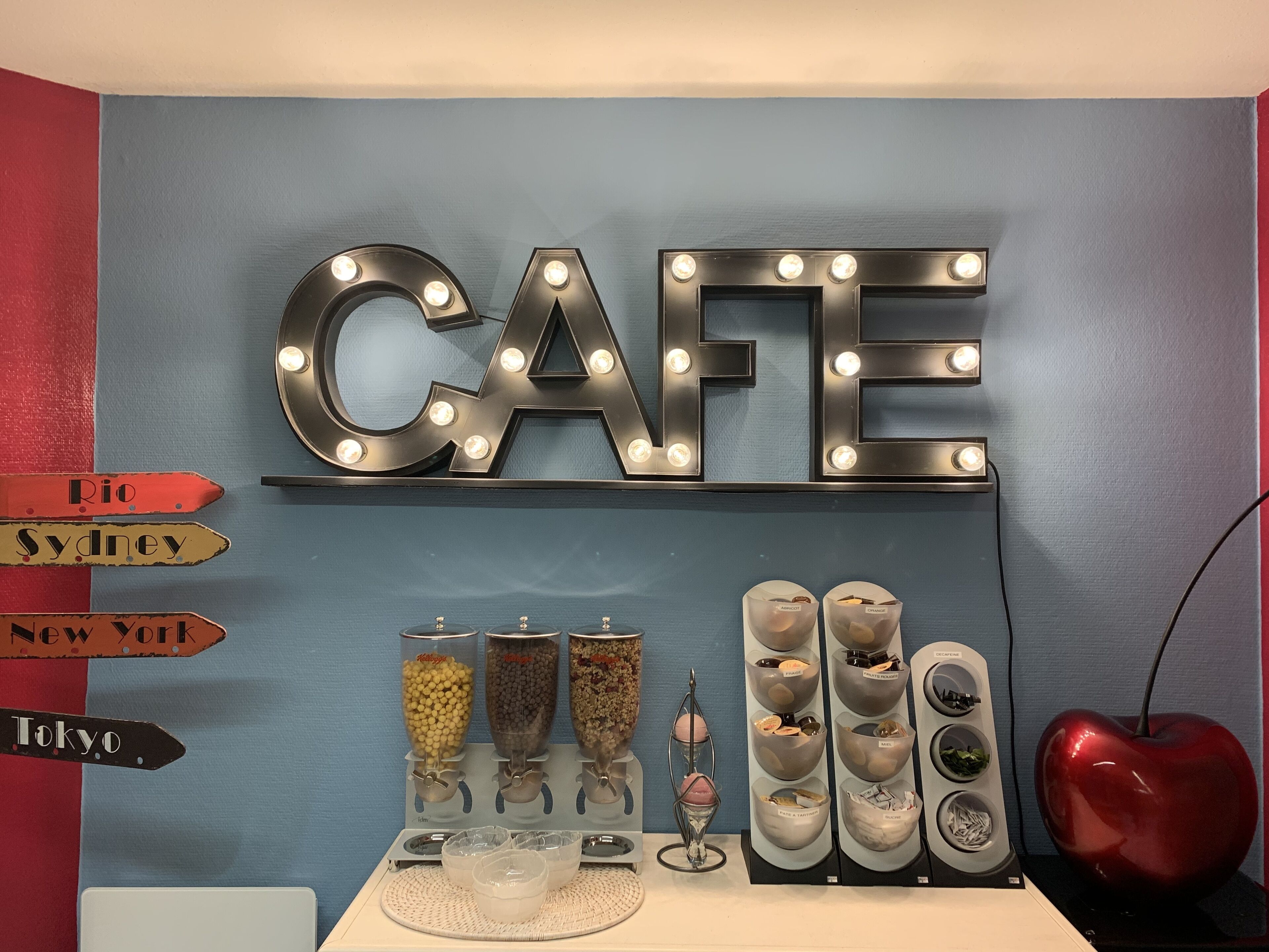A wall with illuminated letters spelling "CAFE" and directional signs pointing to "Rio", "Sydney", "New York", and "Tokyo".