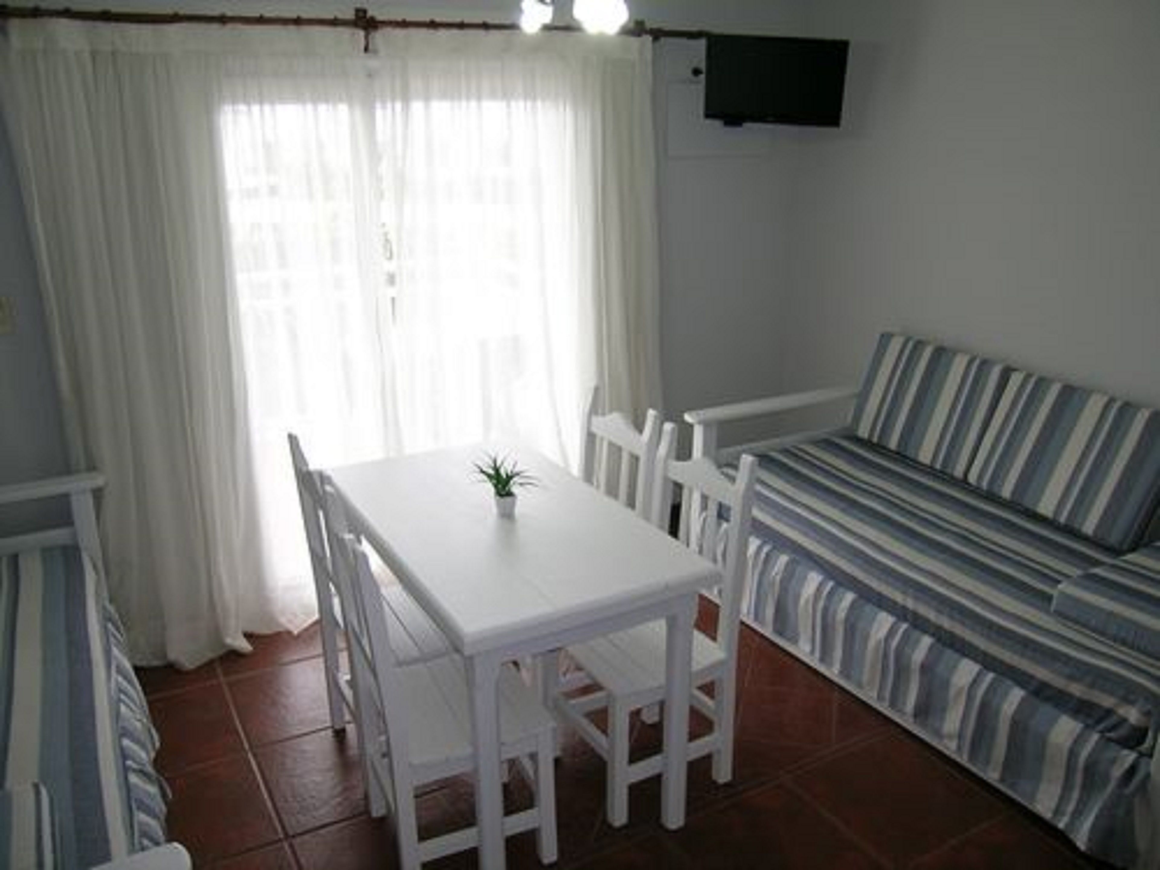 A dining area with a white table and chairs, a striped sofa, and a TV mounted on the wall.