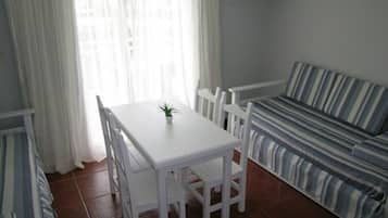 Un coin repas avec une table et des chaises blanches, un canapé à rayures et un téléviseur fixé au mur.