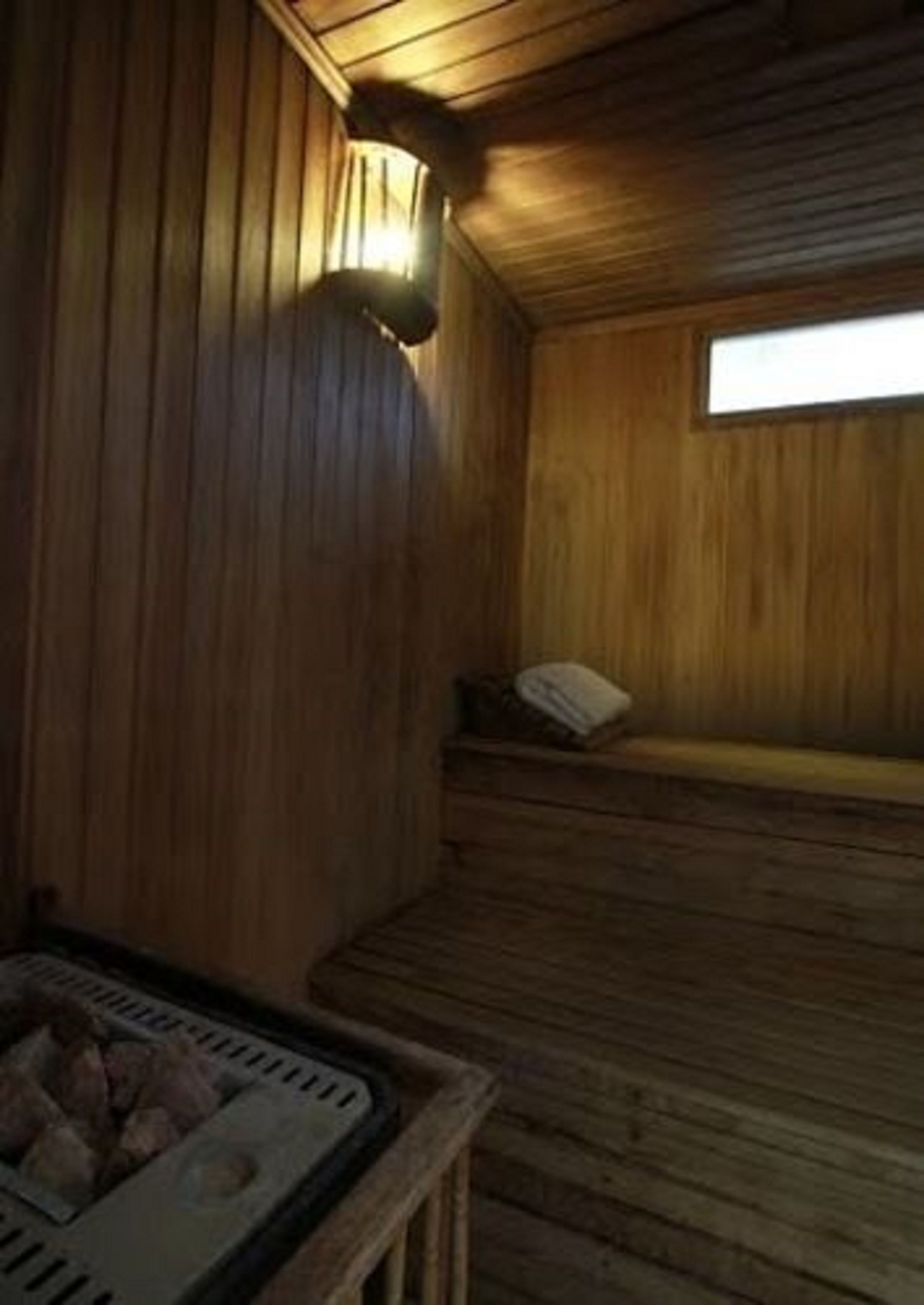 A wooden sauna room with a bench, a small table, and a window providing natural light.