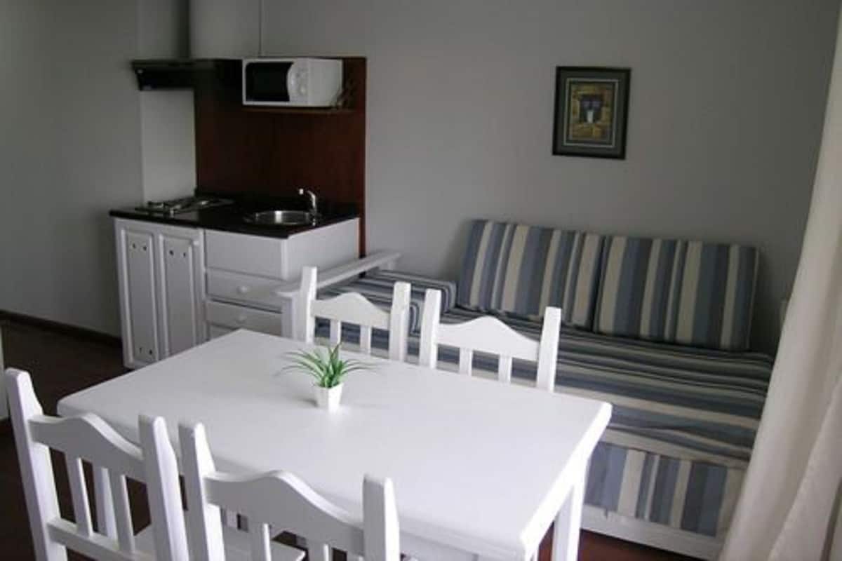 A compact living space with a kitchenette, a dining table with chairs, and a striped sofa.
