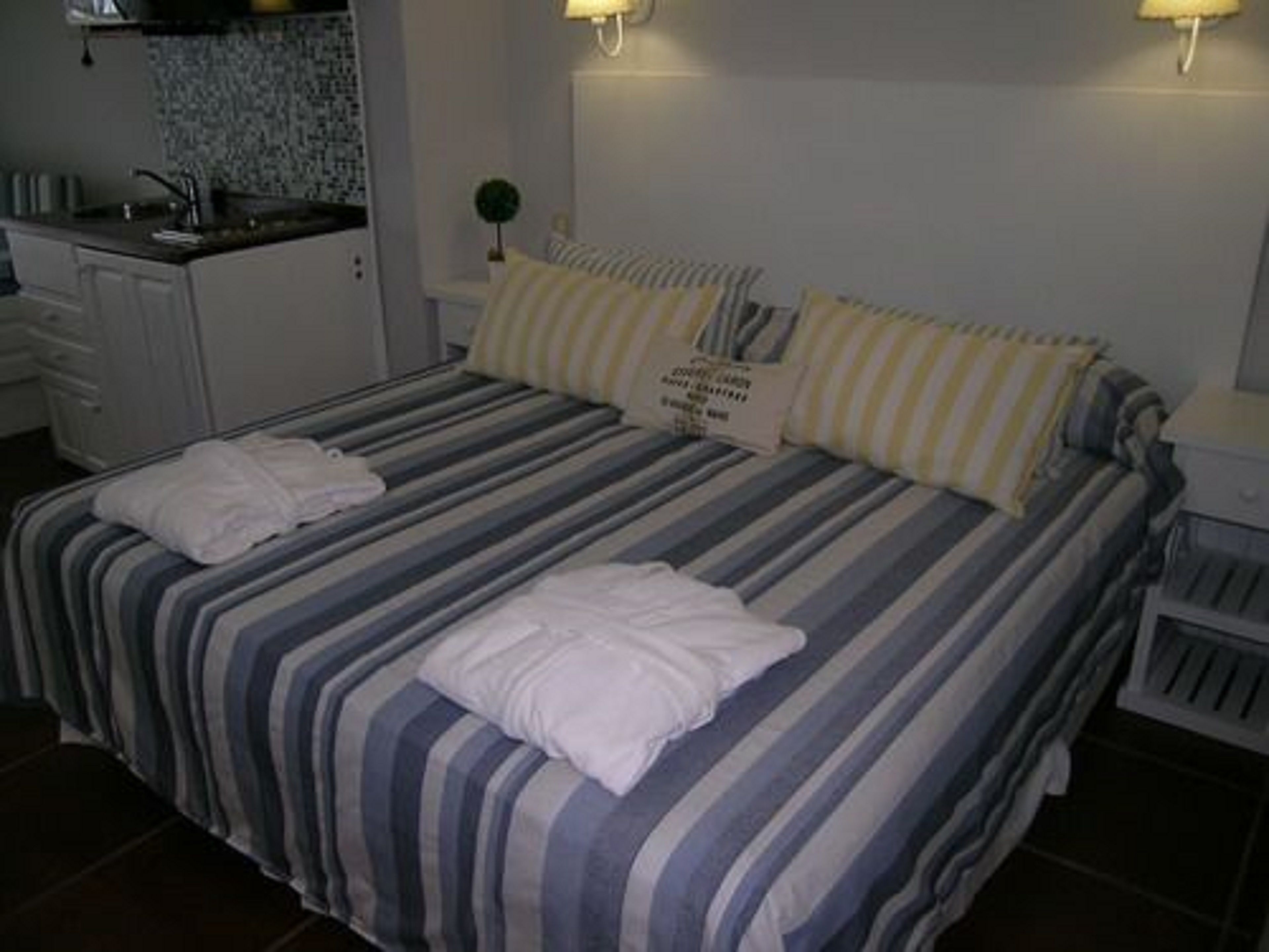 Hotellihuoneessa on sänky, yöpöytä, lamppu, pieni pöytä ja pesuallas huoneen nurkassa.