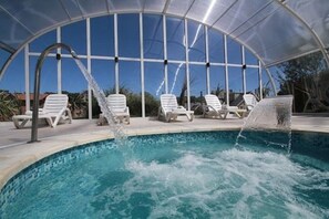 A covered swimming pool with lounge chairs and a water feature.