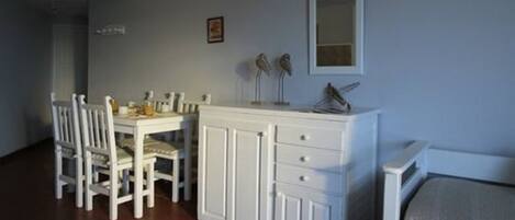 Un coin repas avec une table et des chaises blanches, un meuble blanc avec des tiroirs et un miroir au mur.