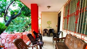 A covered outdoor seating area with plastic chairs and a wooden bench, a red railing, and a tree outside. - Tamarindo hostel (San Pedro Sula)