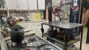 A kitchen with a gas stove, pots, a refrigerator, and various kitchen utensils. - Tamarindo hostel (San Pedro Sula)