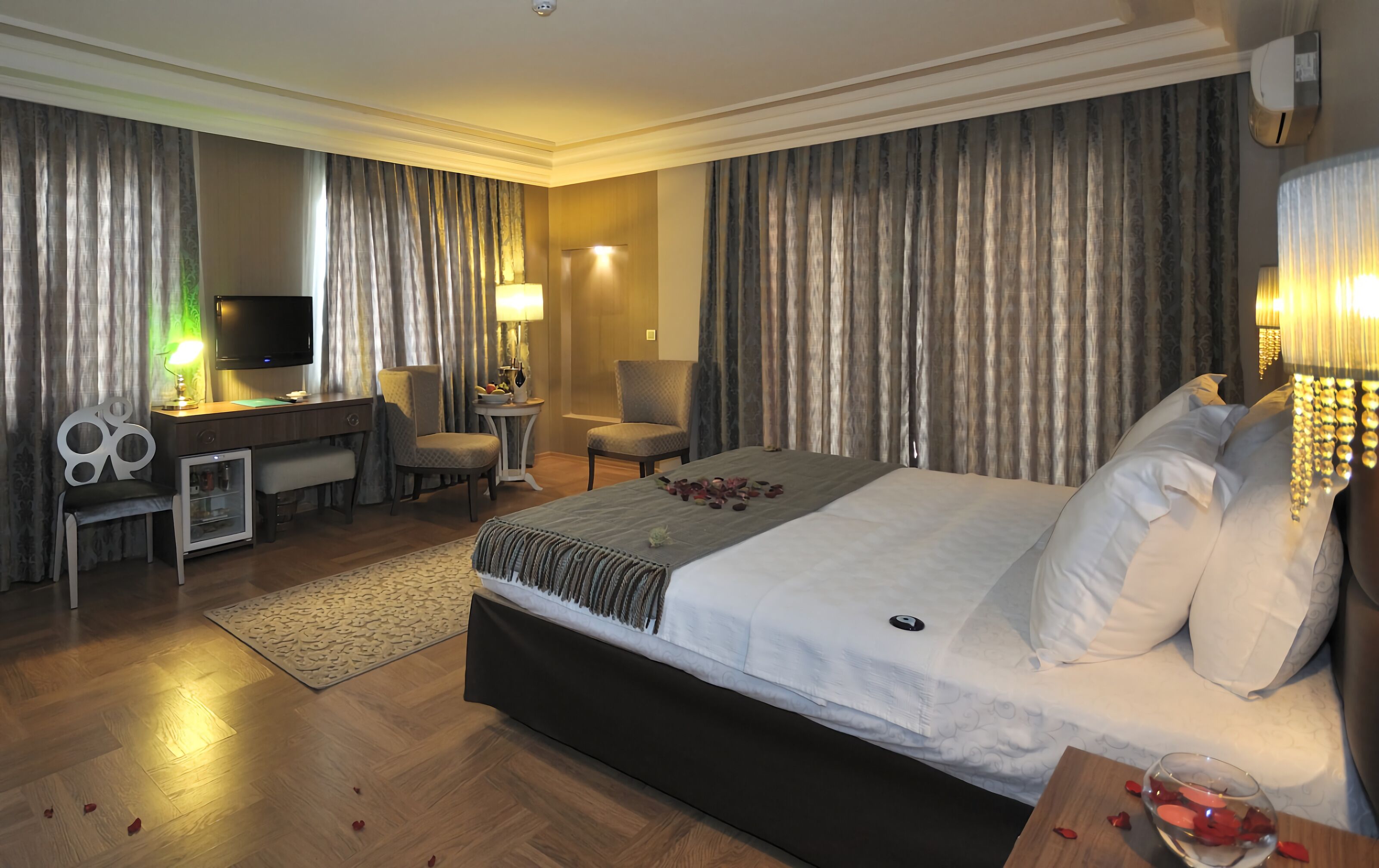 Una habitación de hotel con una cama grande, un escritorio con computadora, una silla, un televisor y una lámpara.