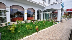 A hotel with a white facade, large arched windows, and a well-maintained garden with potted plants. - Grand Atakum Hotel (Atakum)