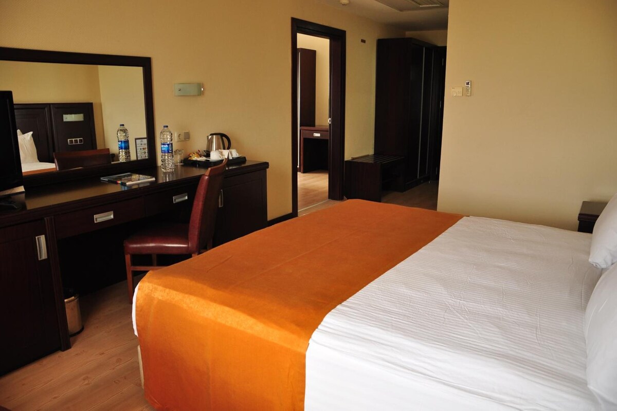 Ein Hotelzimmer mit einem Bett, einem Schreibtisch mit Stuhl, einem Spiegel, einem Fernseher und einer Minibar.