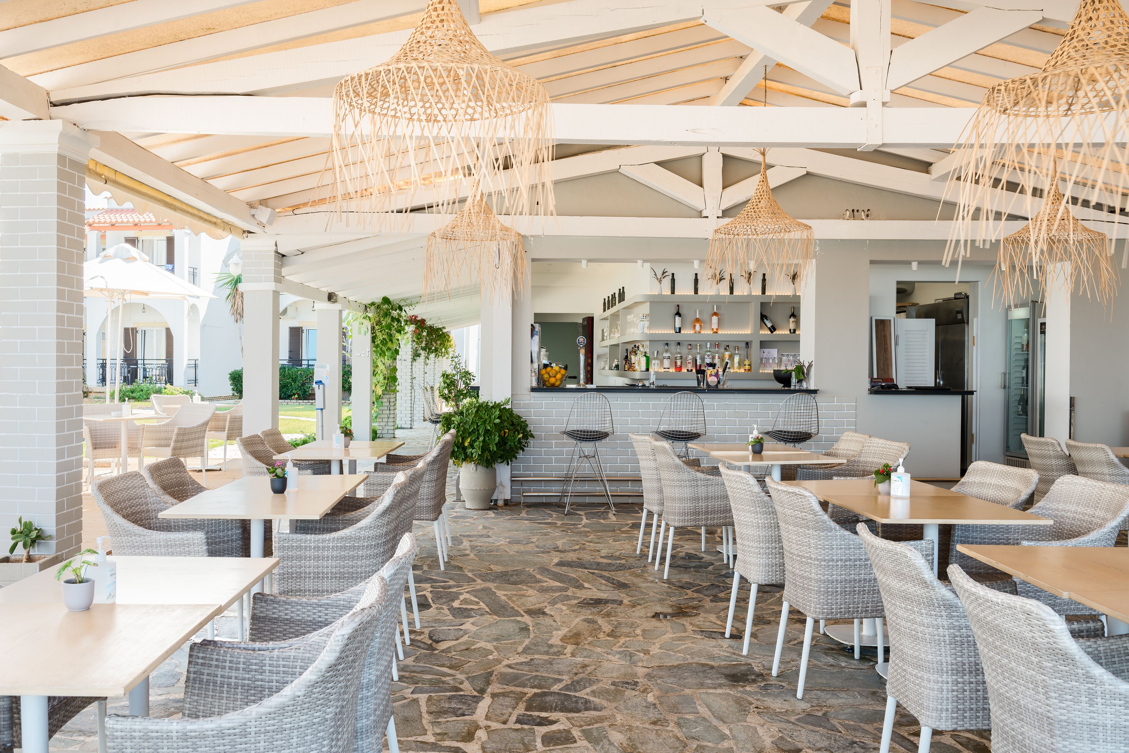 An outdoor cafe with wicker furniture, stone flooring, and hanging wicker lamps.