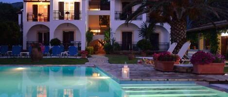 A hotel with a pool, outdoor seating, and a well-lit entrance.