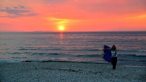 Un coucher de soleil sur l’océan, avec une personne portant une planche de surf bleue.