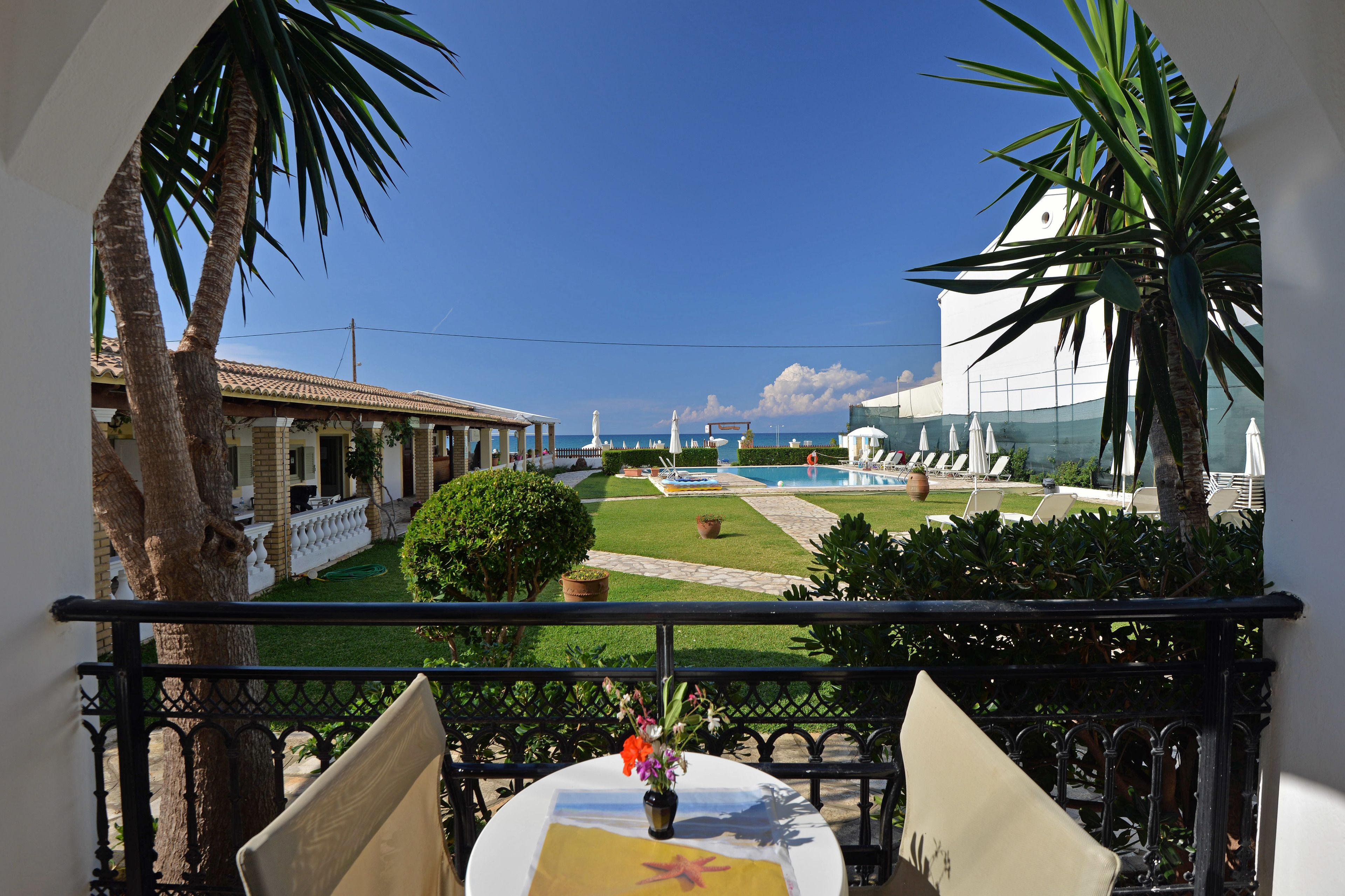 A balcony with a view of a pool, palm trees, and a building with a tiled roof.