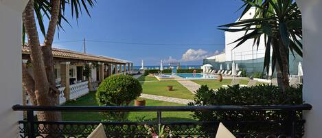 A balcony with a view of a pool, palm trees, and a building with a tiled roof.