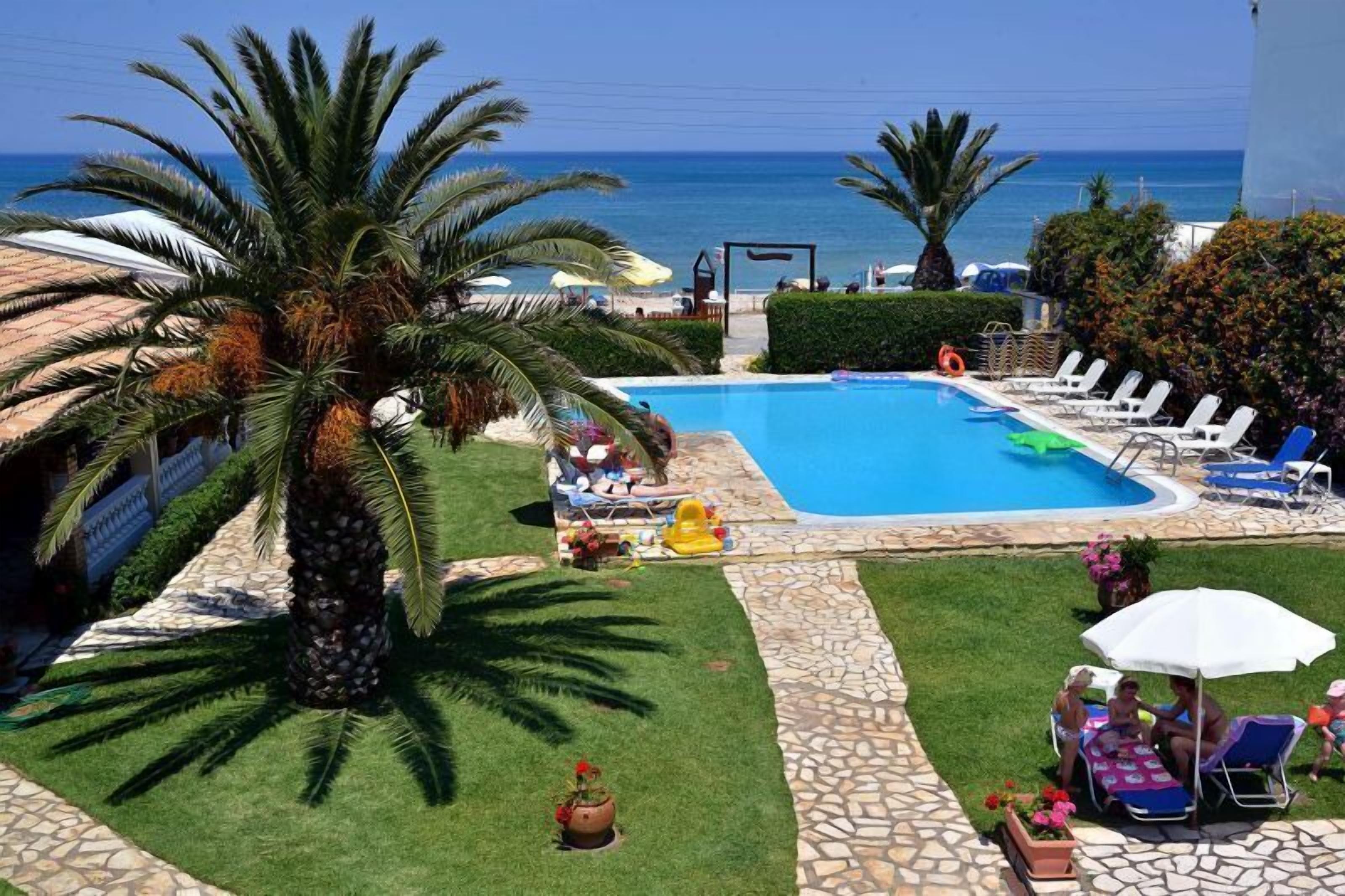 Un espace piscine avec vue sur la mer, entouré de palmiers et de chaises longues.