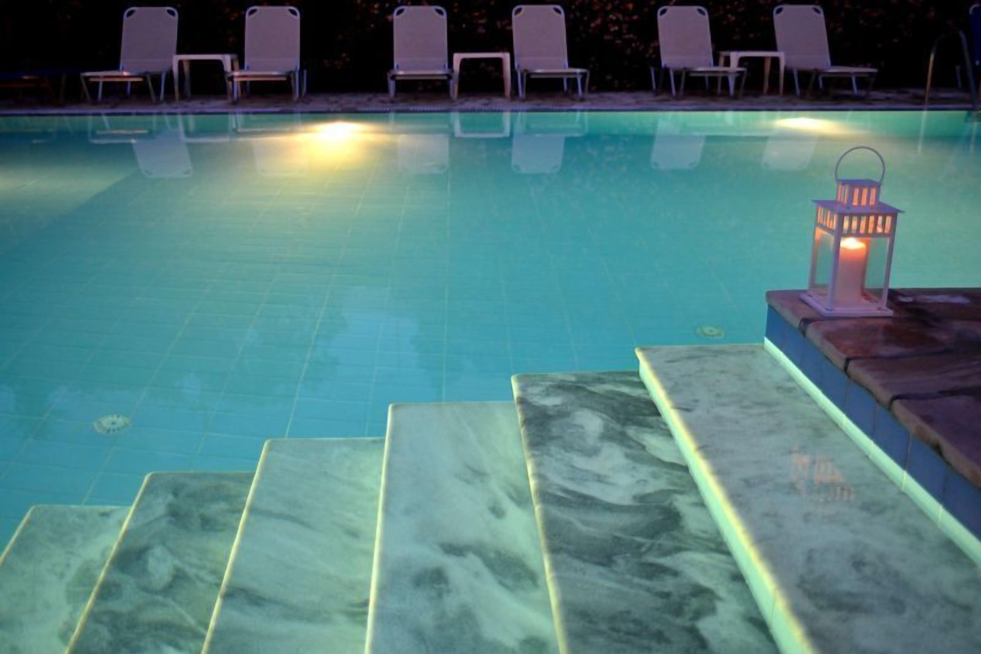 A swimming pool with steps leading down to the water, surrounded by lounge chairs and a lantern.