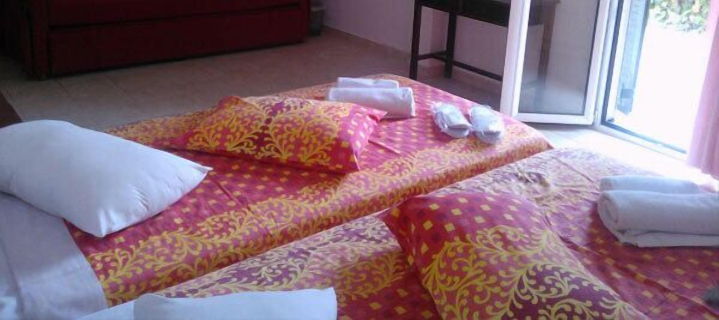 A hotel room with two beds, each with a patterned bedspread, pillows, and rolled towels.