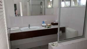 Un baño con lavamanos blanco, un espejo y cabina de ducha de vidrio.