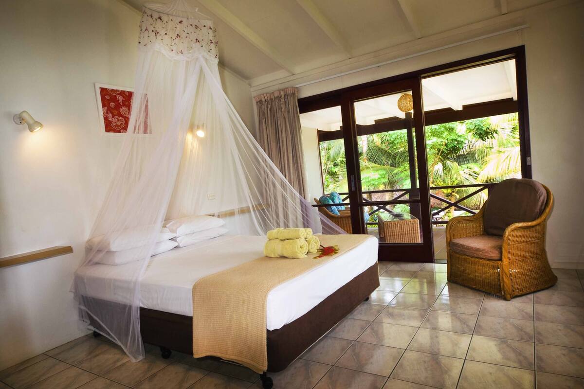 Een slaapkamer met een bed, een stoel en uitzicht op groen.