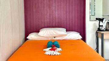 Una cama con una colcha naranja, un cabecero de madera y una pared roja.