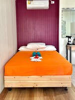 Una cama con una colcha naranja, un cabecero de madera y una pared roja.