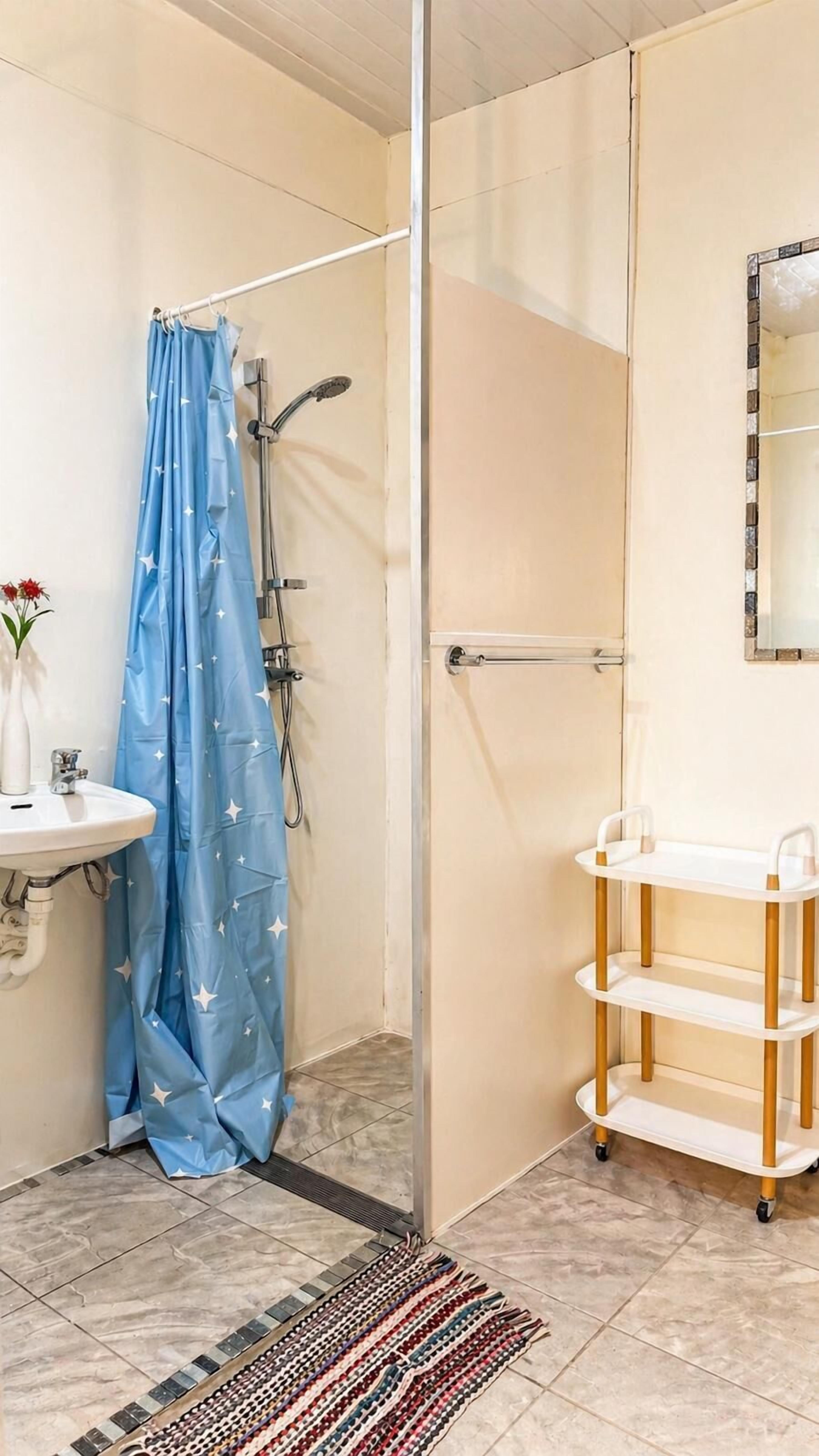 A bathroom with a shower, a sink, a mirror, and a shelf unit.