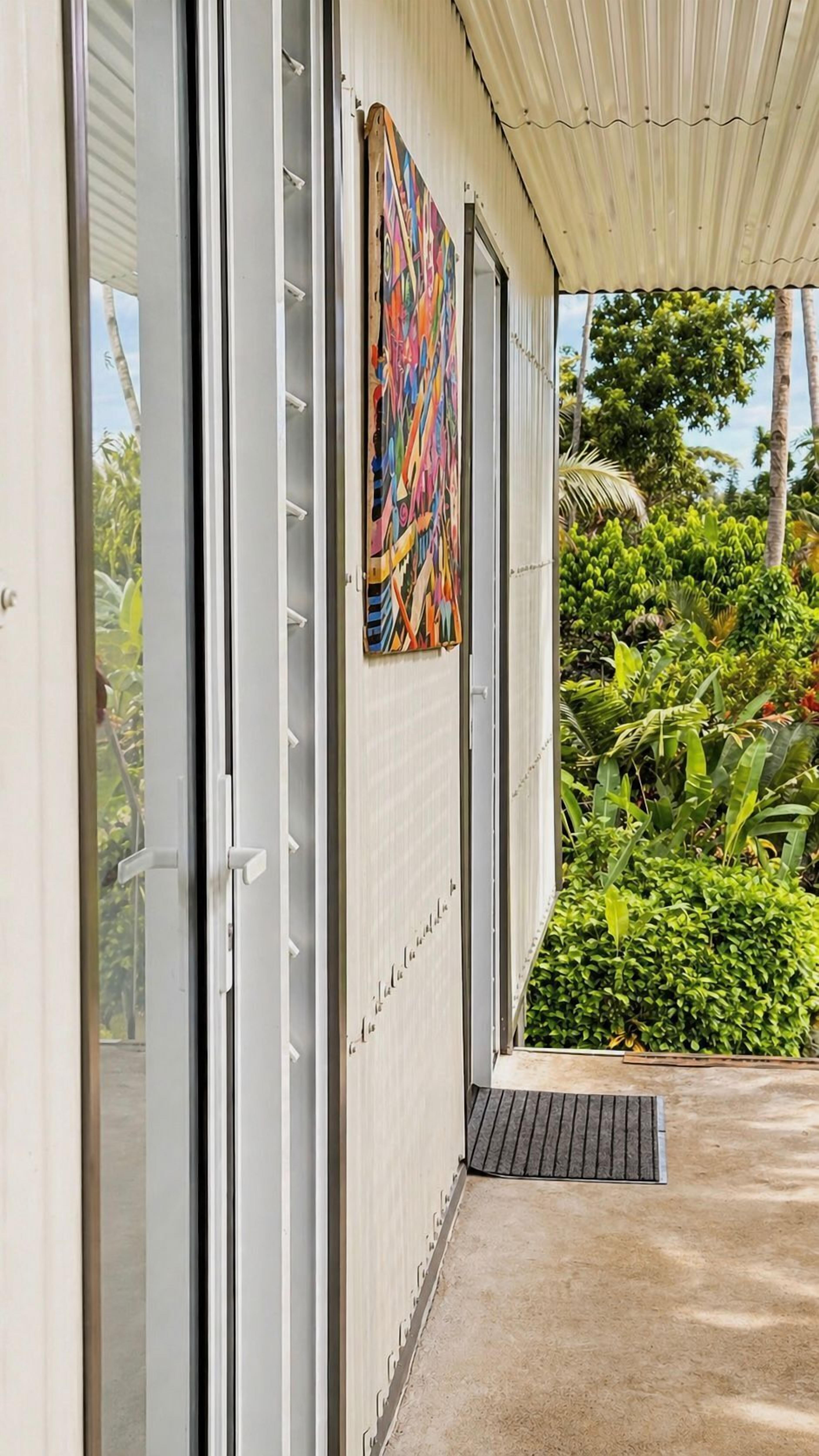A modern building with a sliding glass door, a colorful abstract painting on the wall, and a covered outdoor area with lush greenery.