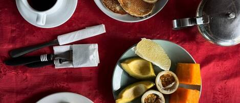 A breakfast setting with toast, pancakes, fruit, and coffee on a red tablecloth.